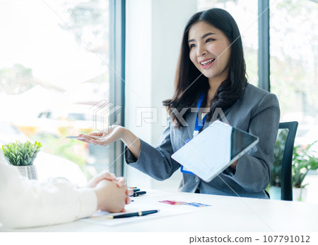 Asian business customer service representatives work and smile serve sell credit card to customers. choosing insurance plan in office Asian business customer service representatives work and smile serve sell credit card to customers. choosing insurance plan in office 107791012