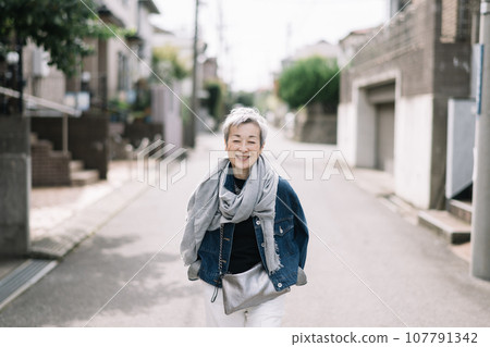 一位優雅的日本女性,頭髮灰白,走在安靜的住宅區 一位優雅的日本女性,頭髮灰白,走在安靜的住宅區 107791342