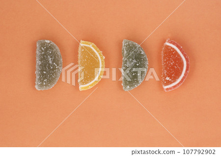 Many multi-colored sweet pieces of marmalade on orange background. 107792902