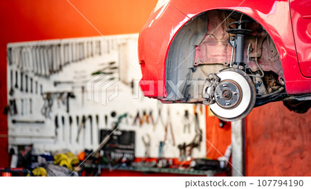 Disc brake component of red car on hydraulic lift Disc brake component of red car on hydraulic lift 107794190