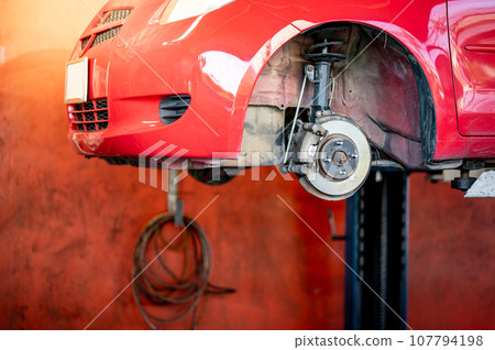 Disc brake component of red car on hydraulic lift Disc brake component of red car on hydraulic lift 107794198