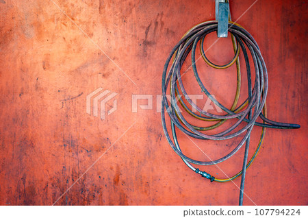 Rolled oil stained air hose reel hanging on an old red wall Rolled oil stained air hose reel hanging on an old red wall 107794224