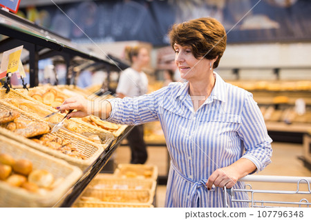 Mature woman examines bakery products in the grocery section of the supermarket 107796348