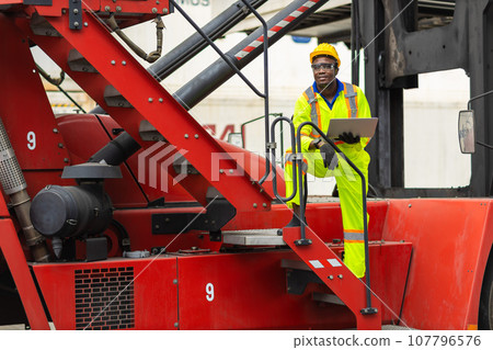 African male dock worker control loading containers cargo at warehouse container shipyard. Marine and carrier staff employee. cargo loading operator shipping export logistics ship yard. African male dock worker control loading containers cargo at warehouse container shipyard. Marine and carrier staff employee. cargo loading operator shipping export logistics ship yard. 107796576