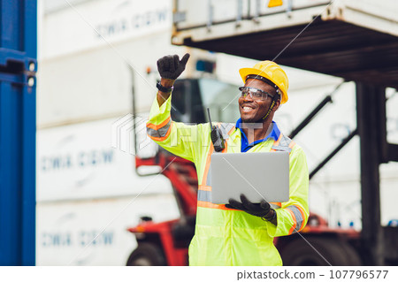 African male dock worker control loading containers cargo at warehouse container shipyard. Marine and carrier staff employee. cargo loading operator shipping export logistics ship yard. 107796577