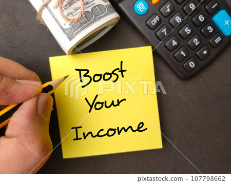 Hand holding pencil with the word Boost your income with banknotes and calculator on black background. 107798662