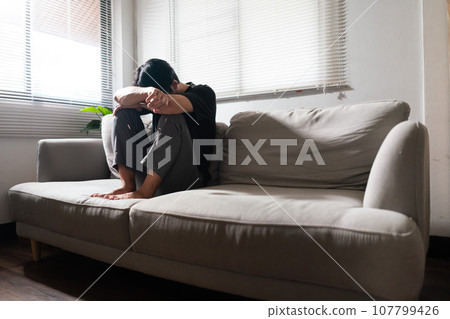 Man with mental health problem sitting on couch to resting head on his arms with depressed emotion Man with mental health problem sitting on couch to resting head on his arms with depressed emotion 107799426
