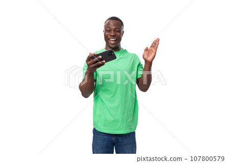 A 30-year-old American man dressed in a light green basic T-shirt is watching a video on a 107800579