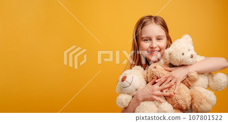 Beautiful girl child with three teddy bears in her hands isolated on yellow background with copyspace. Horizontal portrait of kid holding toys and smiling looking at the camera Beautiful girl child with three teddy bears in her hands isolated on yellow background with copyspace. Horizontal portrait of kid holding toys and smiling looking at the camera 107801522