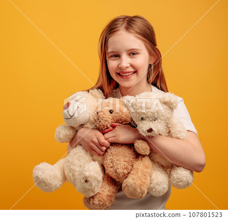 Beautiful girl child with three teddy bears isolated on yellow background with copyspace. Portrait of kid holding toys and smiling looking at the camera Beautiful girl child with three teddy bears isolated on yellow background with copyspace. Portrait of kid holding toys and smiling looking at the camera 107801523