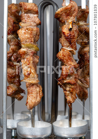 Cooking pork meat in an electric kebab maker on vertical skewers 107801839