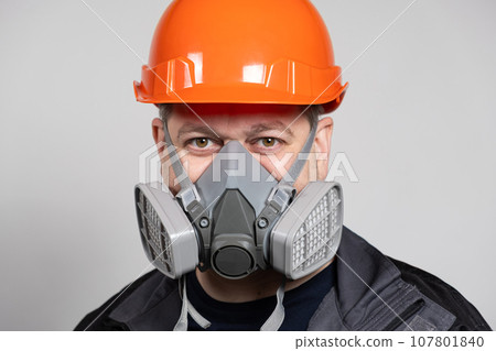 A man wearing a safety helmet and a respirator to protect against dust and gases on a white background. 107801840