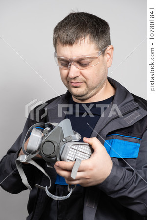 A man holds a respirator half mask to protect against dust and gases. 107801841