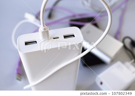 Power bank, external battery and usb wire on the table, universal mobile battery for charging gadgets, for recharging a smartphone 107802349
