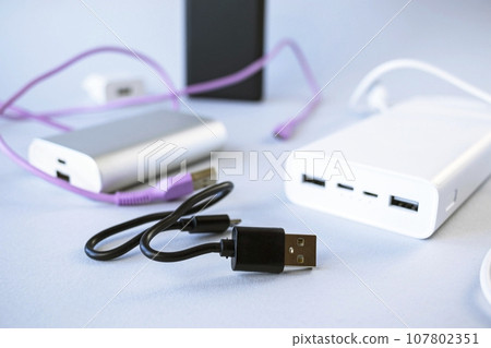 Power bank, external battery and usb wire on the table, universal mobile battery for charging gadgets, for recharging a smartphone Power bank, external battery and usb wire on the table, universal mobile battery for charging gadgets, for recharging a smartphone 107802351