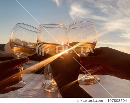 A group of friends raise a toast with glasses of white wine, sunset . A group of friends raise a toast with glasses of white wine, sunset . 107802704