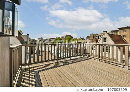 a wooden deck with houses in the background and blue sky above it, as seen from an outdoor patio area 107803809