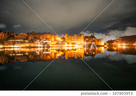 Stunning views of Udaipur City Palace at night from Lake Pichola. 107803953