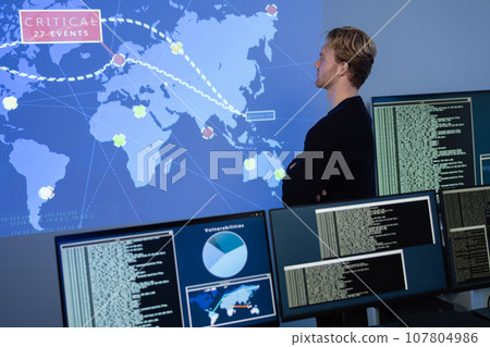 Back View in the Cyber Security Control Center Operator Working. Multiple Screens Showing Technical Data and Alerts. 107804986