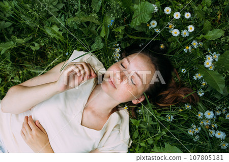 Beautiful woman with natural beauty without makeup lies in the grass in summer Beautiful woman with natural beauty without makeup lies in the grass in summer 107805181