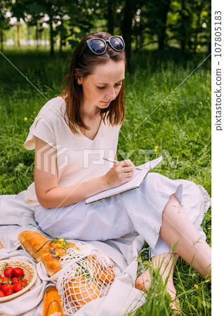 Beautiful woman on picnic. She smiles, eats strawberries and enjoys summer. 107805183