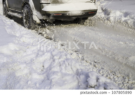 Road snow flies up from a vehicle's spinning wheel. Car's wheels spin and spew up pieces of snow it attempts to gain traction on the slippery road. Road snow flies up from a vehicle's spinning wheel. Car's wheels spin and spew up pieces of snow it attempts to gain traction on the slippery road. 107805890