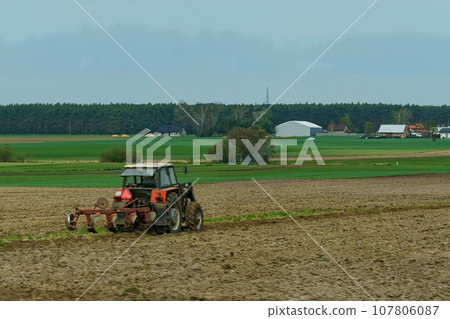A tractor with plows stands near a plowed field. 107806087