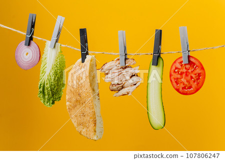 Doner kebab with ingredients hanging on a thread in the air : beef meat, lettuce, onion, tomatoes, cheese, cucumber. Yellow background 107806247