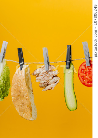 Doner kebab with ingredients hanging on a thread in the air : beef meat, lettuce, onion, tomatoes, cheese, cucumber. Yellow background Doner kebab with ingredients hanging on a thread in the air : beef meat, lettuce, onion, tomatoes, cheese, cucumber. Yellow background 107806249