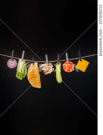 Doner kebab with ingredients hanging on a thread in the air : beef meat, lettuce, onion, tomatoes, cheese, cucumber. Black background 107806252