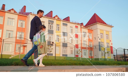 father escorts his little daughter with backpack school lesson. happy family. Parents children walk hand hand school. fun approach learning. happy father little first-grader. conversation with father. 107806580