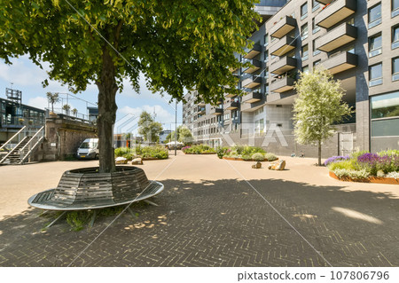 a bench in the middle of an urban area with trees and plants on either side of the street there is a blue sky above 107806796