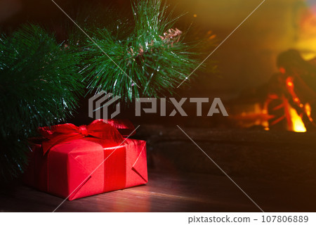 Christmas composition, gift under the tree near a burning fireplace, close-up Christmas composition, gift under the tree near a burning fireplace, close-up 107806889