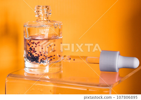 Hyaluronic acid in a glass bottle with a pipette on an orange background against wet glass. Facial Serum or cuticle oil in a bathroom. Hydro boost serum provides active moisturizing for aging skin. 107806895