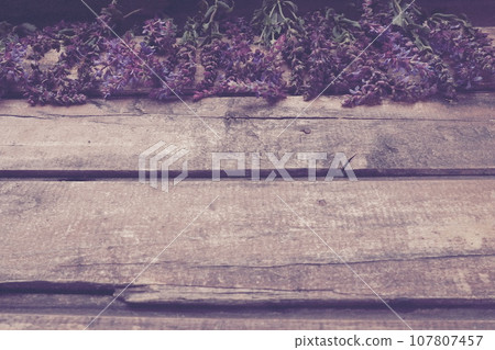 Lavender and sage flowers on a wooden table close-up. Horizontal planks of dark old wood with purple and blue flowers and leaves around the edges. Still life and flat lay. Free copy space for text 107807457