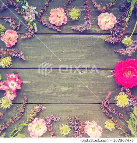 Flowers in a circle on a wooden background. Postcard for the holiday. Roses, geraniums, lavender, sage and hairy chestnuts are placed along the edges on dark boards. Background copy space, flat lay. Flowers in a circle on a wooden background. Postcard for the holiday. Roses, geraniums, lavender, sage and hairy chestnuts are placed along the edges on dark boards. Background copy space, flat lay. 107807475