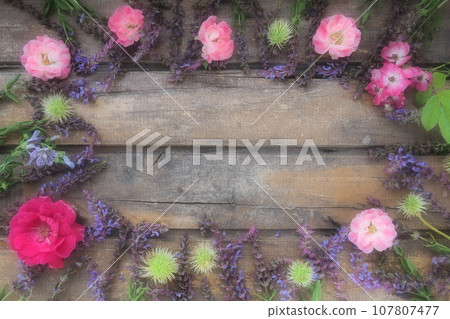 Flowers in a circle on a wooden background. Postcard for the holiday. Roses, geraniums, lavender, sage and hairy chestnuts are placed along the edges on dark boards. Background copy space, flat lay. 107807477