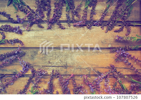 Lavender and sage flowers on a wooden table close-up. Horizontal boards of dark old wood with purple and blue flowers and leaves all around. Still life and flat lay. Free space for text. Copy space. 107807526