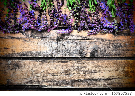 Lavender and sage flowers on a wooden table close-up. Horizontal planks of dark old wood with purple and blue flowers and leaves around the edges. Still life and flat lay. Free copy space for text 107807558