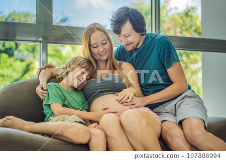 Expectant parents, mom, dad, and their eldest son share a heartwarming moment on the sofa, discussing the exciting journey of pregnancy 107808994