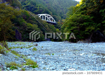 View of the white railing of Hiwata Bridge from the wide riverbed of the Kanno River 107809431