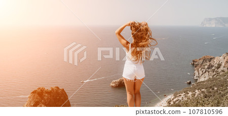 Woman summer travel sea. Happy tourist enjoy taking picture outdoors for memories. Woman traveler posing over sea bay surrounded by volcanic mountains, sharing travel adventure journey 107810596