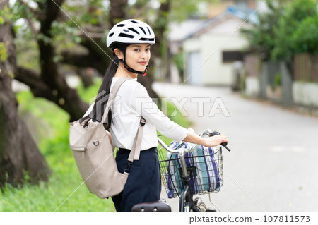A young woman wearing a cycling helmet and walking with a bicycle A young woman wearing a cycling helmet and walking with a bicycle 107811573