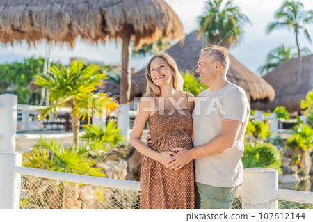 A happy, mature couple over 40, enjoying a leisurely walk in a park, their joy evident as they embrace the journey of pregnancy later in life 107812144
