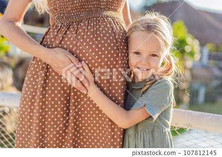 A heartwarming moment captured as a daughter lovingly embraces her mother's pregnant belly, sharing in the excitement and anticipation of a new family member A heartwarming moment captured as a daughter lovingly embraces her mother's pregnant belly, sharing in the excitement and anticipation of a new family member 107812145