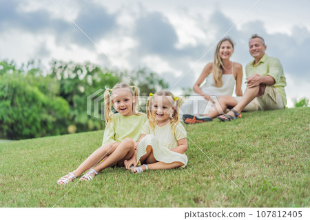 A happy family, two girls, dad, and a pregnant mom, enjoys quality time together on a lush green lawn, creating cherished memories of togetherness 107812405