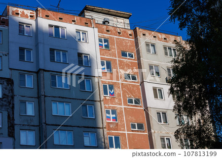 typical russian ugly high rise apartmant building with russian national flags in some windows at summer day 107813199