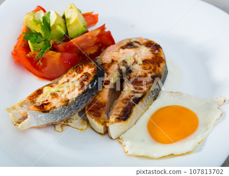 Fried salmon on white plate with fried egg, tomatoes, avocado Fried salmon on white plate with fried egg, tomatoes, avocado 107813702