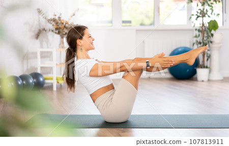 Young woman yoga trainer performing boat pose on black rug 107813911