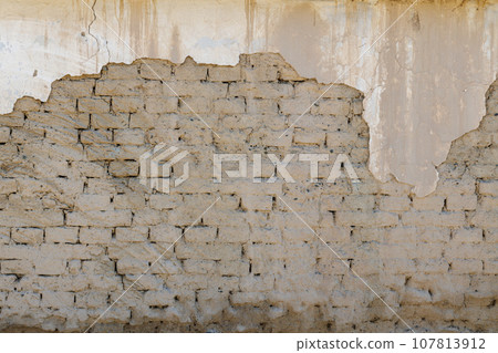 old adobe building wall with peeled off plaster 107813912